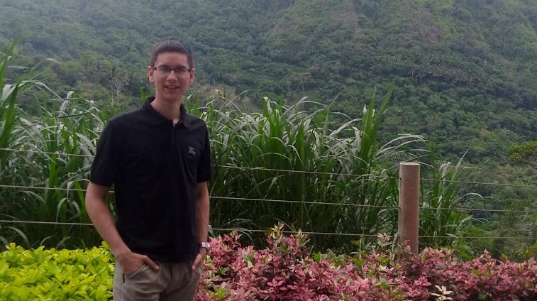 Alum Raphael Roxas in a polo and shorts standing in front of a green field and hills. Alum Raphael Roxas in a polo and shorts standing in front of a green field and hills.